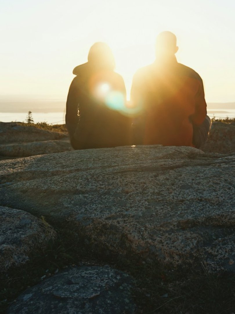 Two people sitting together watching the sunrise from a hilltop - partnership and leadership journey